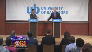 Reps. Donna Edwards and Chris Van Hollen standing behind podiums with a sign behind saying University of Baltimore