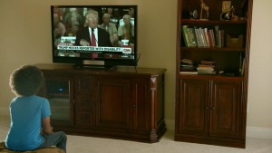 17-year-old Dante Latchman sitting in his living room watching TV, which shows Donald Trump allegedly mocking a journalist with a disability