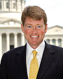 Official portrait of Chris Koster  in a black suit, white shirt and yellow tie