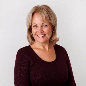Headshot of Kathy Szeliga in a dark top against a gray background, smiling and facing camera