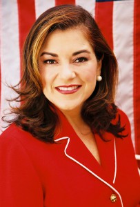 Headshot of Loretta Sanchez in a red suit with American flag as backdrop