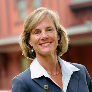 headshot of Sue Minter in a white shirt and blue blazer, outside with building behind her