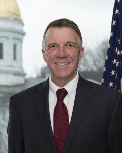 Vermont Governor Phil Scott smiling in front of an American flag and the state legislature