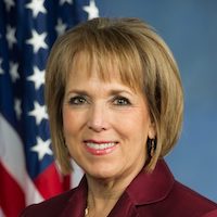 New Mexico Governor Michelle Lujan Grisham smiling in front of an American flag