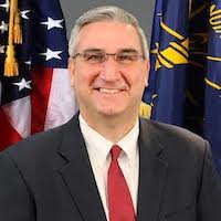 Indiana Governor Eric Holcomb smiling in front of the American flag and the state flag
