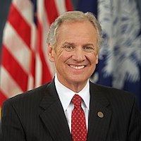 Governor Henry McMaster smiling in front of an American flag and the South Carolina state flag
