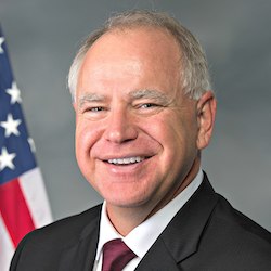 Governor Tim Walz smiling in front of an American Flag