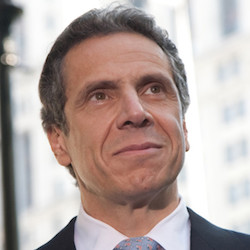 Governor Andrew Cuomo smiling in front of a blurred background of buildings