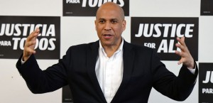 Booker smiles with his arms outstretched in front of campaign signs that read, "Equal Justice for All" in English and Spanish.
