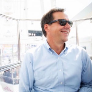 Steve Bullock wearing sunglasses and a blue button down shirt, smiling and looking to his lef