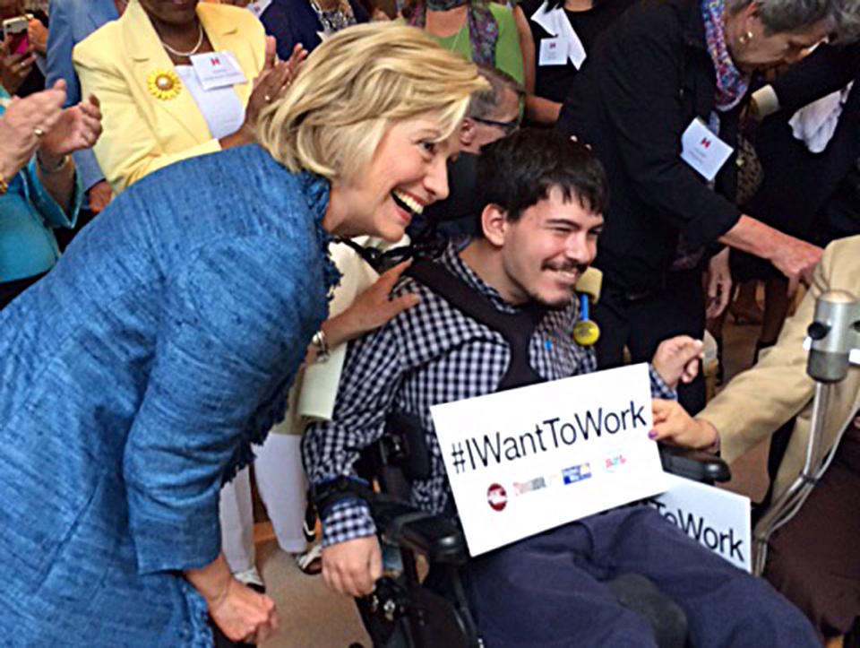 Hillary Clinton with a supporter in a wheelchair with a sign saying #IWantToWork