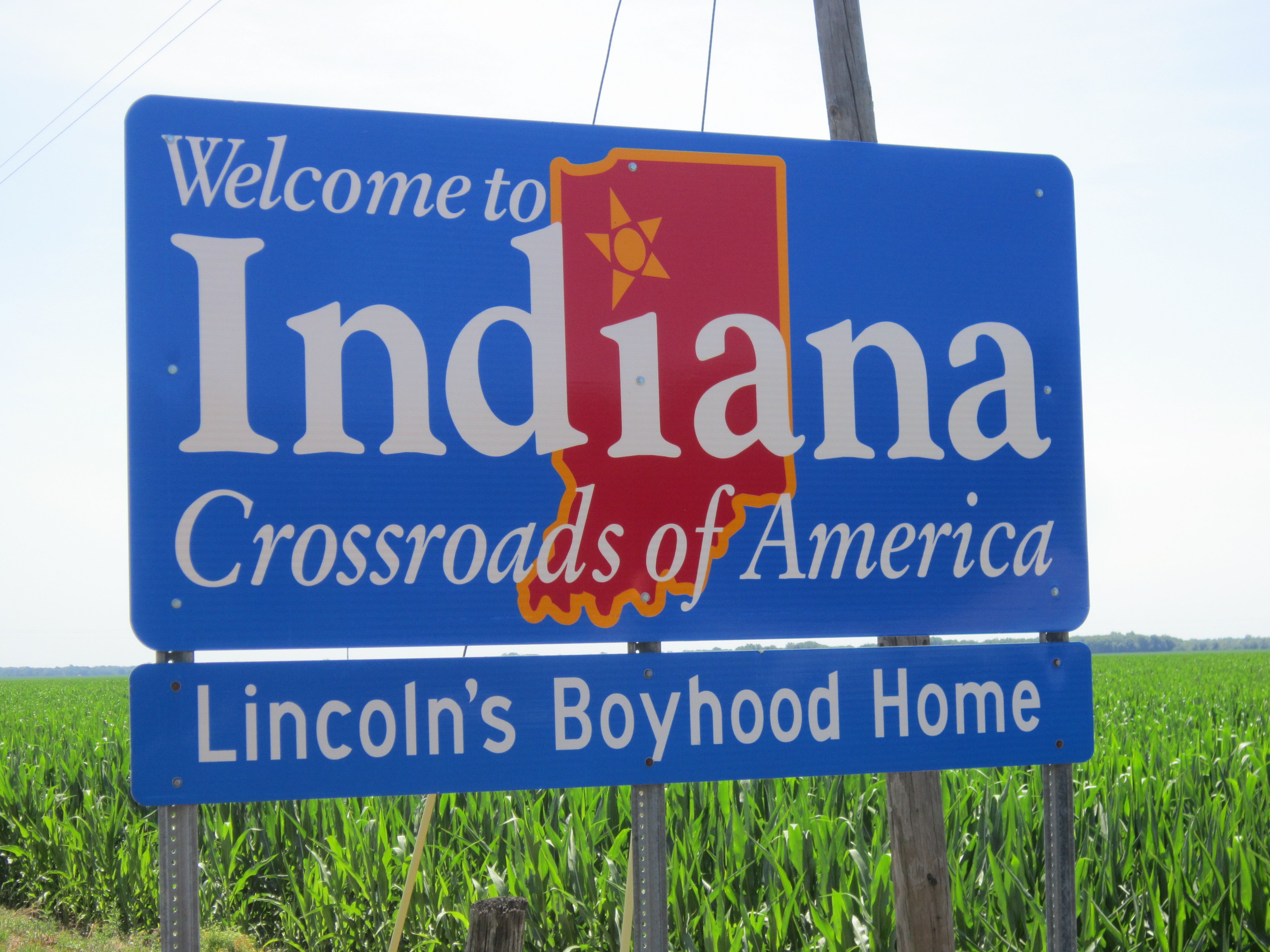 Indiana Road Sign on side of a road in a field, text on sign: Welcome to Indiana, crossroads of America, Lincoln's boyhood home