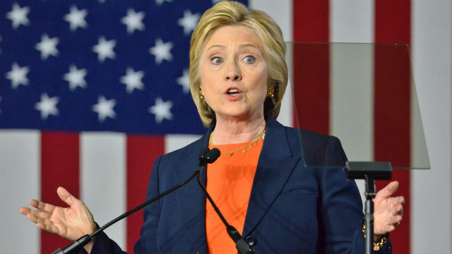 Close-up of Hillary Clinton talking behind a podium in front of a large American flag