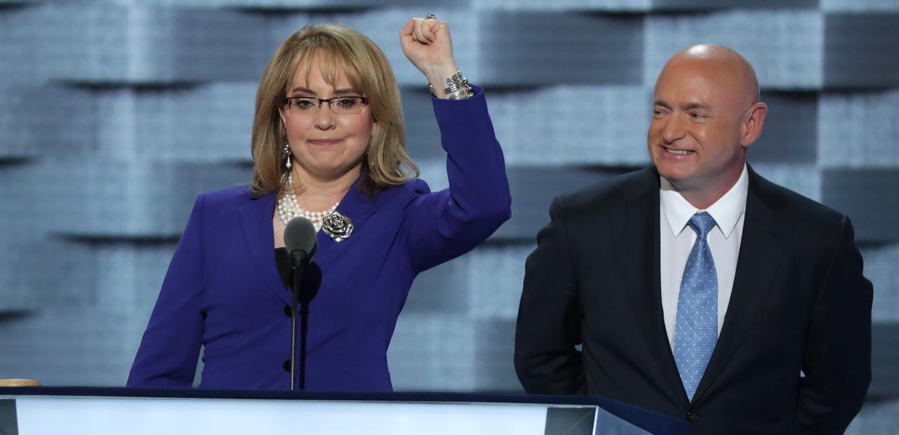 Image of Gabby Giffords raising left arm enthusiastically with husband Mark Kelly standing next to her