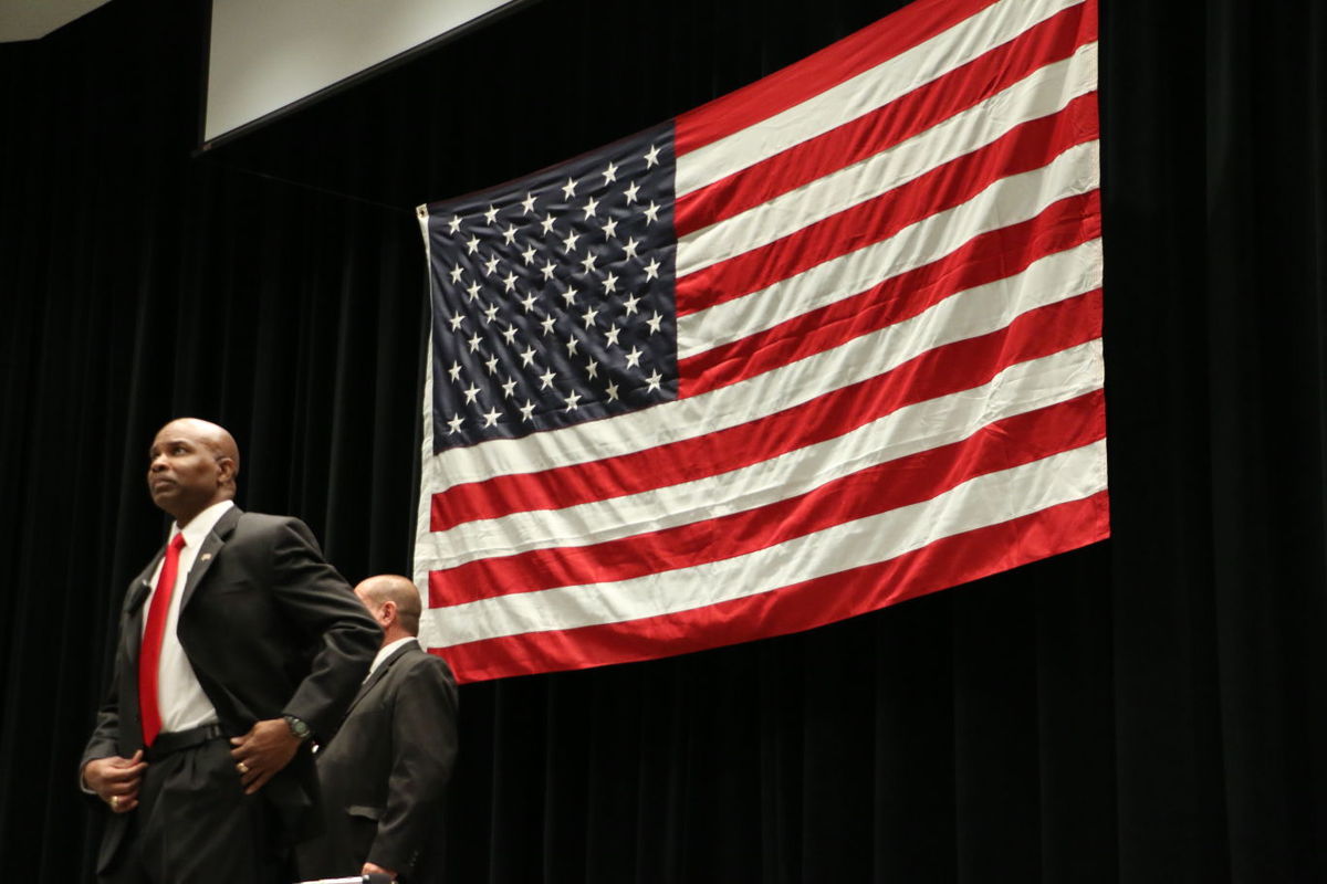 Dwight Young standing on a stage with a large American flag in the background