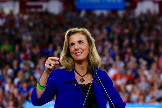 Katie McGinty speaking at a Hillary Clinton rally wearing a blue suit and large crowd behind her