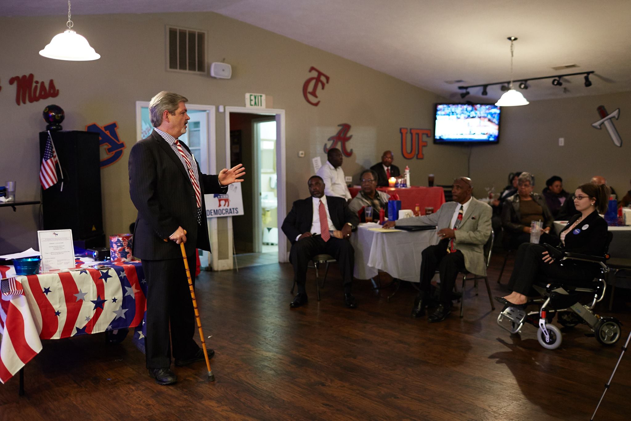 Ron Crumpton speaking at a campaign event. He is using a cane and there is a woman in a wheelchair in the audience.
