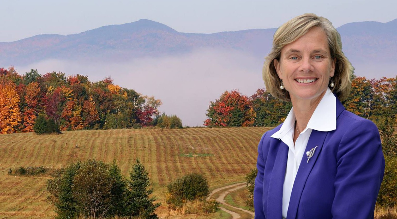 Sue Minter standing in a white shirt and blue blazer with a field behind her