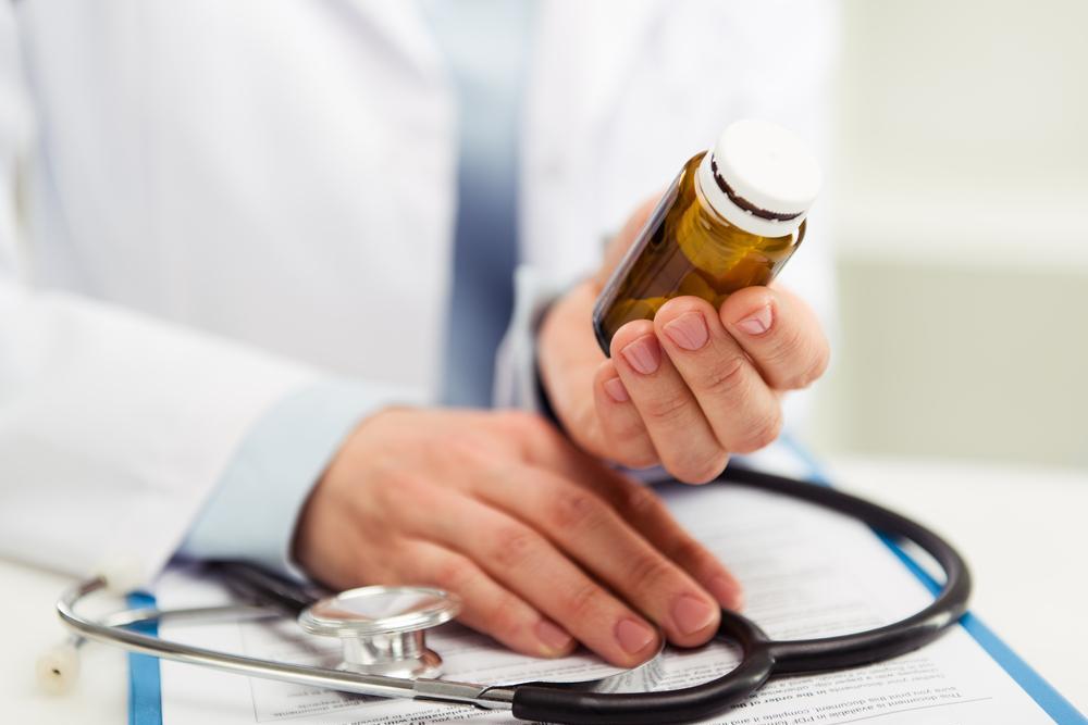 Image of a doctor's hands holding a stethoscope and bottle of medicine