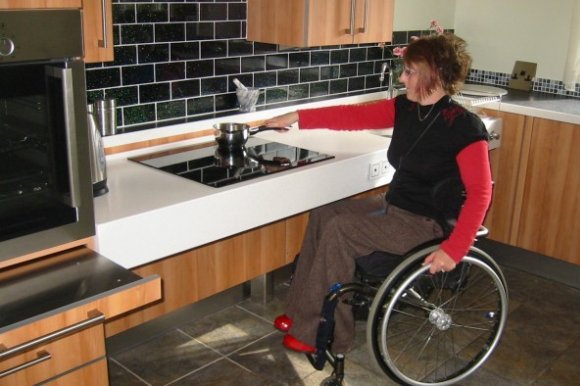 A young woman in a wheelchair using a stovetop in an accessible kitchen