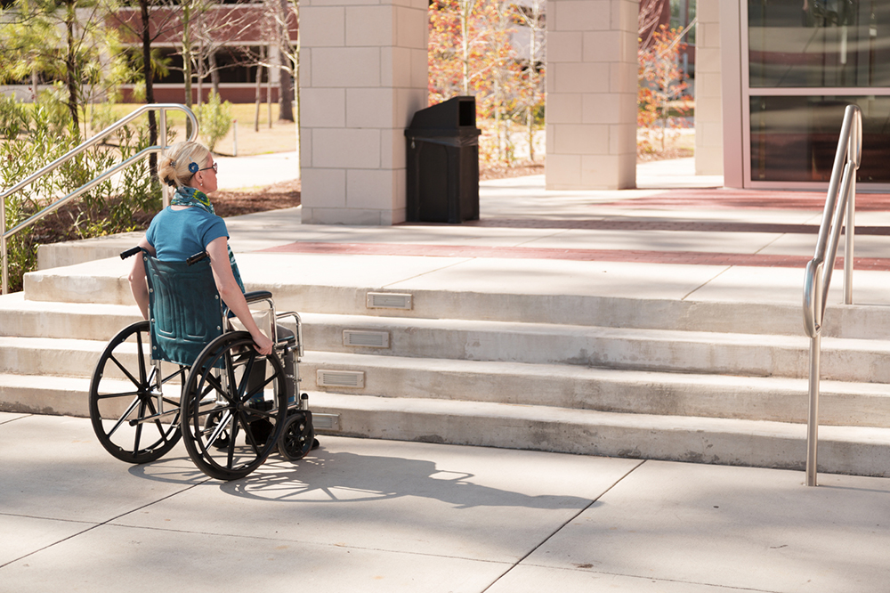 A young woman in a wheelchair looks up at in lack of an accessible entrance - only stairs
