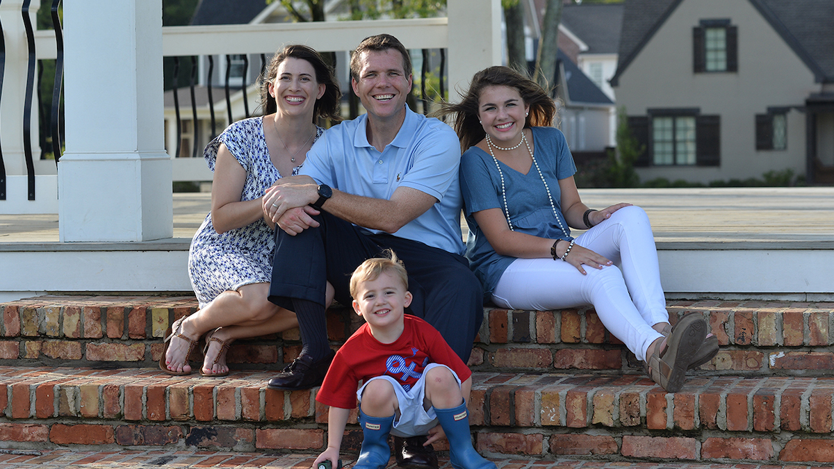 Walt Maddox and his family sit and smile on steps to their house