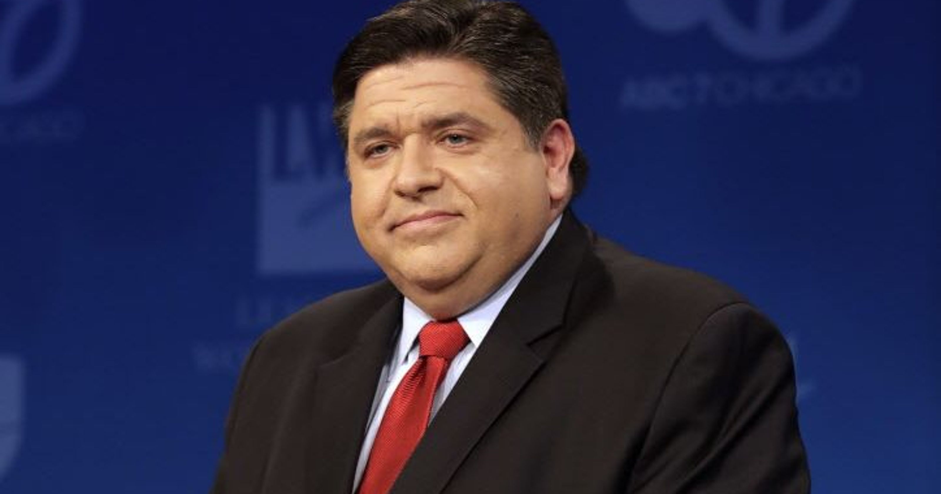 JB Pritzker in a suit with a blue blurred background behind him