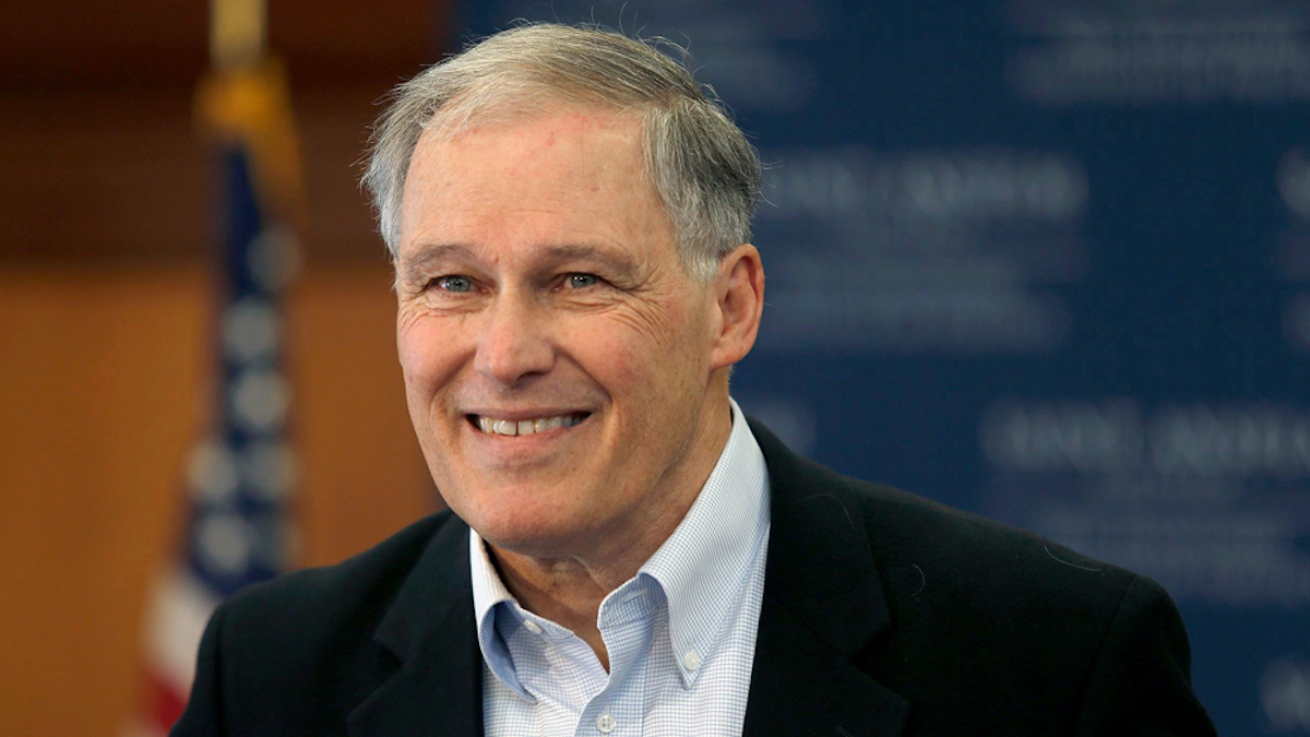 Jay Inslee in front of a blurred background of an American flag and a blue wall