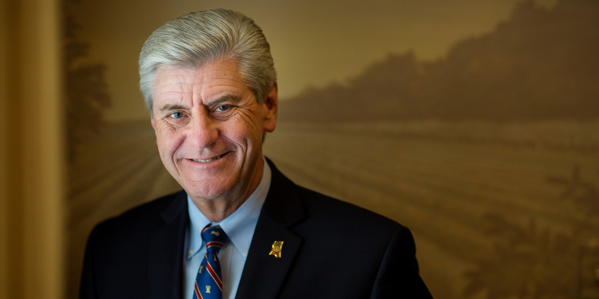 Governor Phil Bryant smiling in front of a painting of mountains
