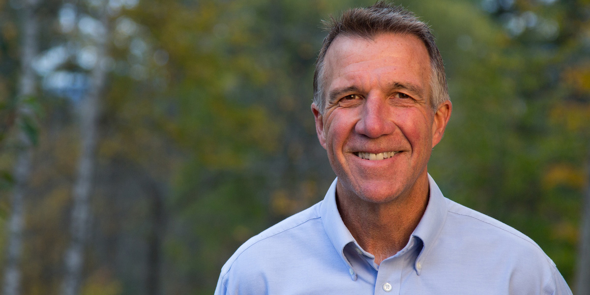 Governor Phil Scott smiles in front of blurred trees in the background