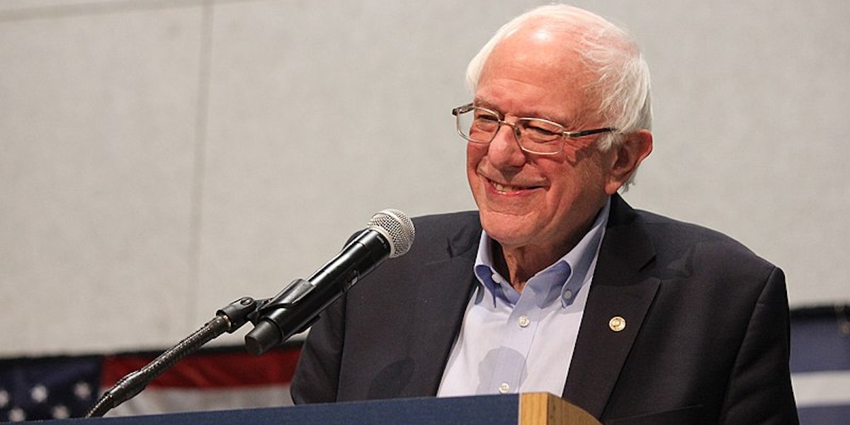Bernie Sanders smiling behind a microphone and podium.