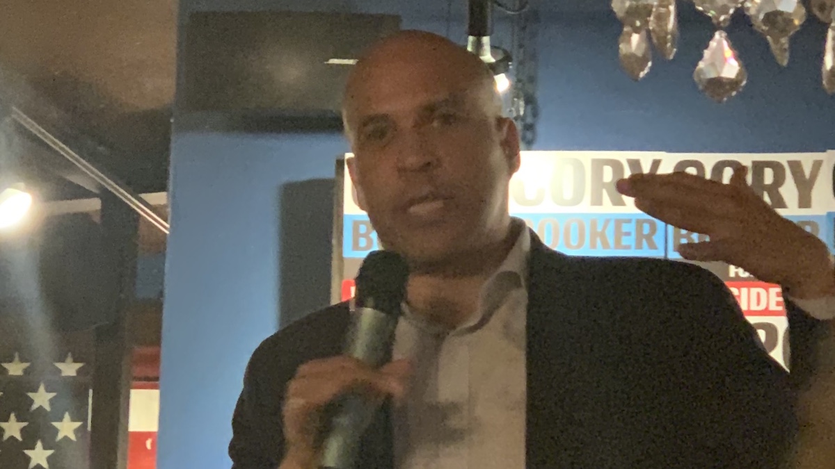 Cory Booker speaks at an event in Washington, D.C. in front of signs for his campaign and an American flag