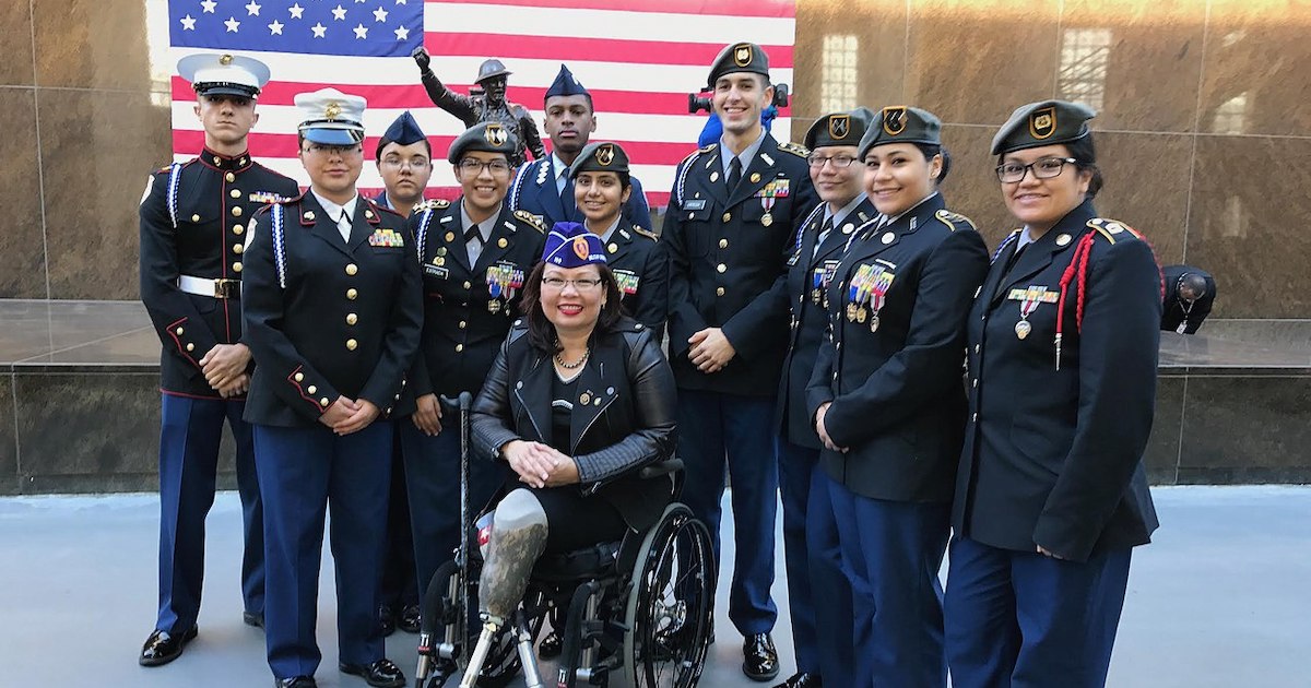 Tammy Duckworth with a group of other veterans smiling in front of an American Flag