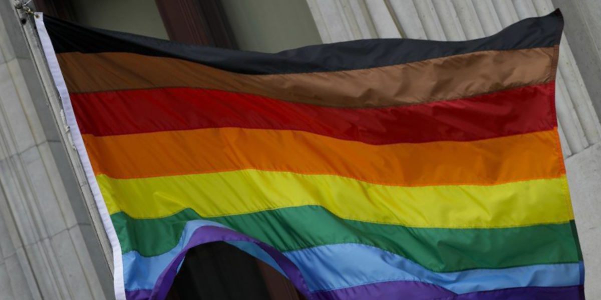 an LGBTQ+ Pride flag with black, brown, red, orange, yellow, green, blue and purple stripes
