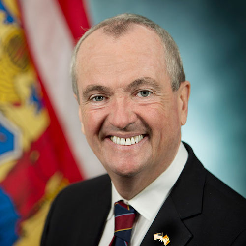 Phil Murphy smiling in front of the New Jersey flag