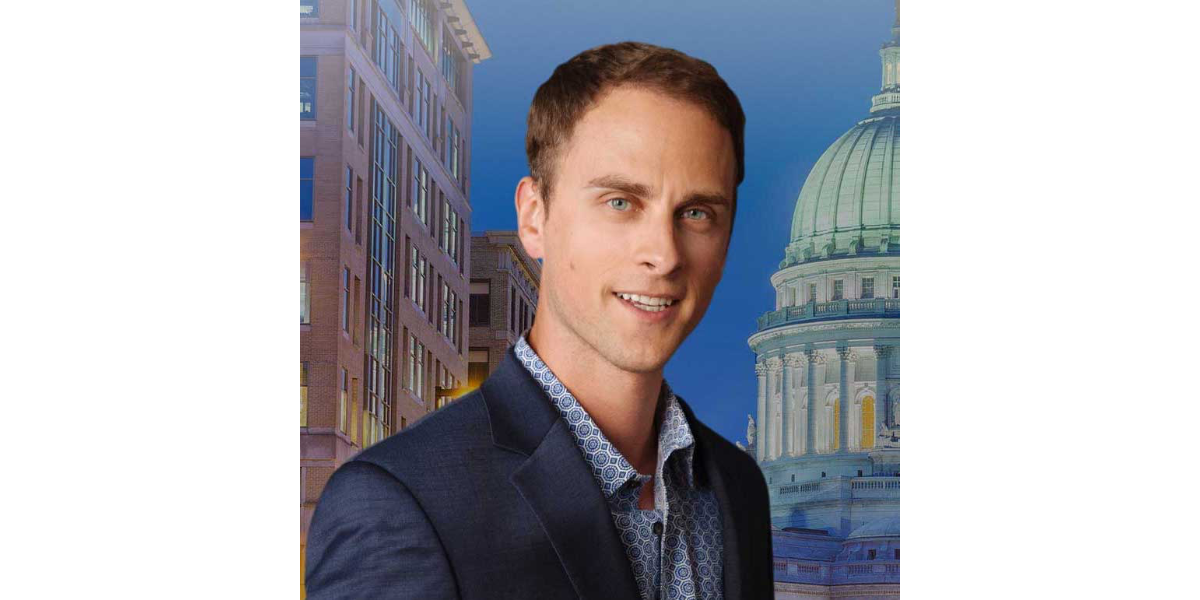 Johnathan Wichmann headshot wearing a suit in front of a backdrop of a capitol building