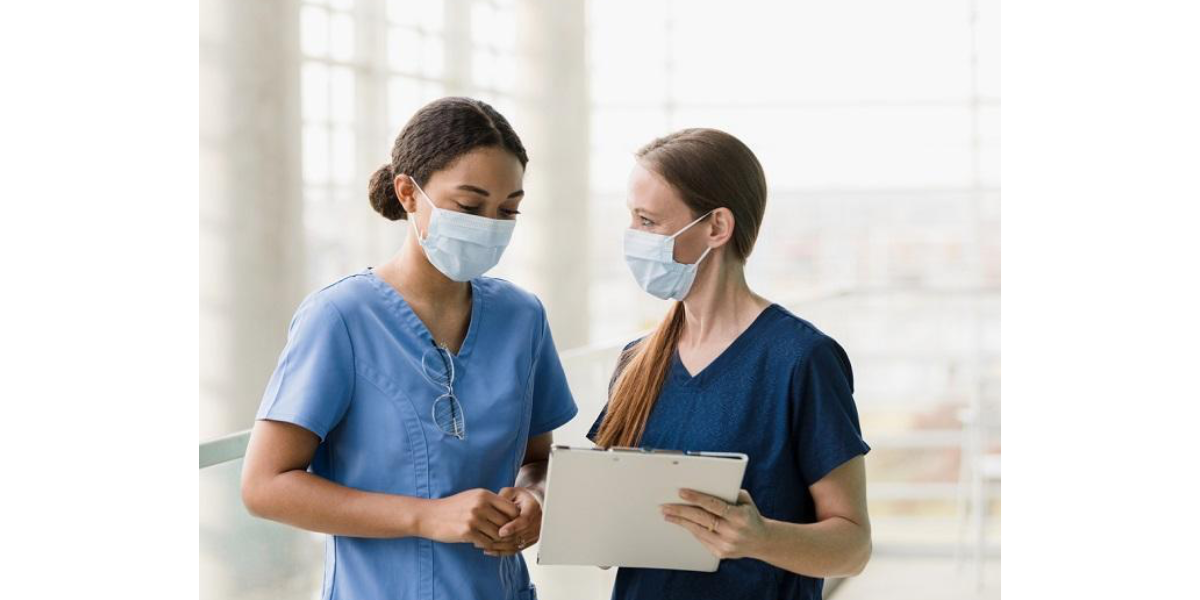 Two health care workers wearing masks and scrubs looking at a document together